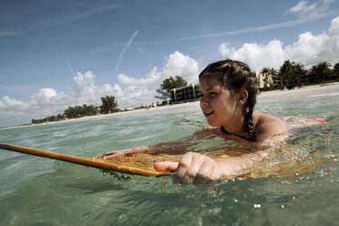 A young girl boogie boards in the ocean with blue skies and clouds in the background. - AURF04260