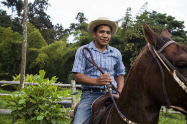 A young man sits on a horse and smiles on a coffee farm in Colombia. - AURF04269