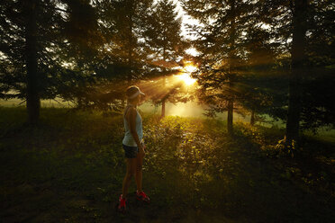 Eine Läuferin unterbricht ihren Lauf, um den Sonnenaufgang zu genießen, der durch die Bäume scheint. - AURF04399