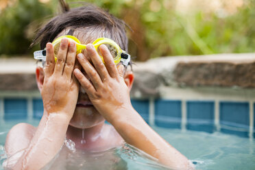 Ein Junge schwimmt in einem Pool und bedeckt sein Gesicht und seine Brille mit seinen Händen - AURF04413
