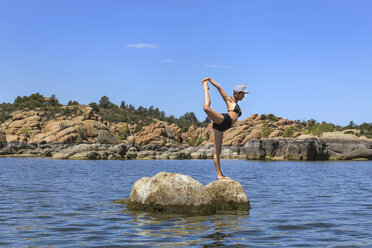 Eine flexible und sportliche junge Frau posiert auf einem Felsen in einem See - AURF04434