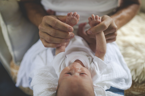 Ein Vater hält zärtlich die Hände seines neugeborenen Babys, lizenzfreies Stockfoto