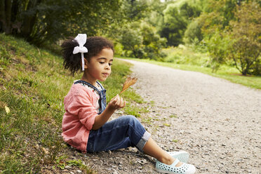 Ein kleines Mädchen sitzt auf der Seite der Straße und hält ein Herbstblatt - AURF04482