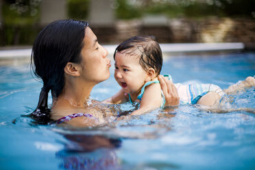 Eine japanisch-amerikanische Mutter schwimmt und hält ihr 10 Monate altes Mädchen in einem Schwimmbad. - AURF04489