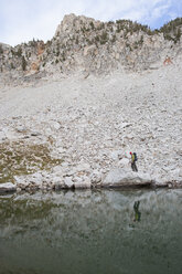 A man walking a rocky shorline under a mountain. - AURF04522