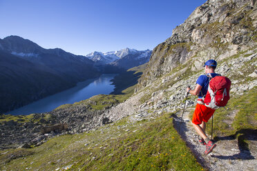 A solo male hiker enjoying the view over Lac des Dix in Val d'H├â┬®r├â┬®mence, in the Swiss Alps. - AURF04532
