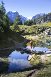 Ein alleinreisender männlicher Wanderer geht über eine Brücke im Blauen See oberhalb von Arolla in den Schweizer Alpen. - AURF04535