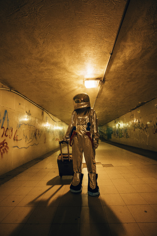 Raumfahrer in der Stadt bei Nacht in einer Unterführung mit Rollkoffer stehend, lizenzfreies Stockfoto