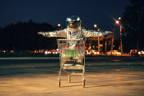 Raumfahrer in der Stadt bei Nacht auf einem Parkplatz in einem Einkaufswagen - VPIF00680