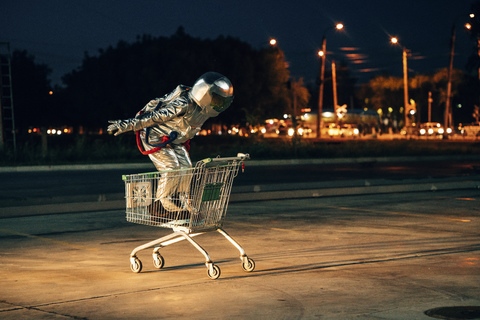 Raumfahrer in der Stadt bei Nacht auf einem Parkplatz in einem Einkaufswagen, lizenzfreies Stockfoto