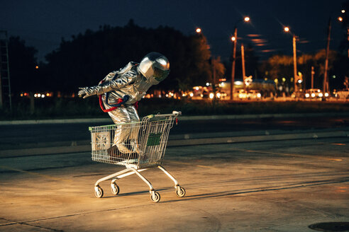 Spaceman in the city at night on parking lot inside shopping cart - VPIF00681