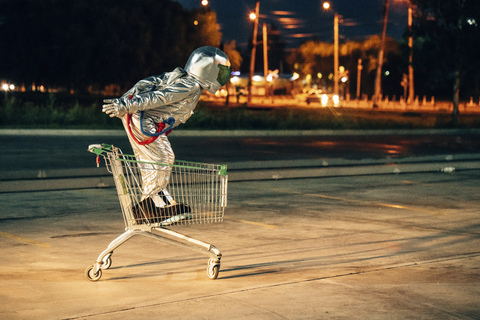 Spaceman in the city at night on parking lot inside shopping cart stock photo