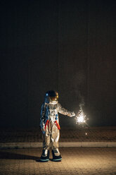 Raumfahrer steht nachts auf einer Straße und hält eine Wunderkerze - VPIF00706
