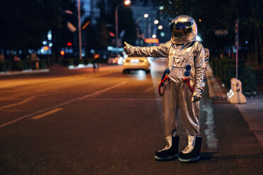 Spaceman standing on a street in the city at night hitchhiking - VPIF00716