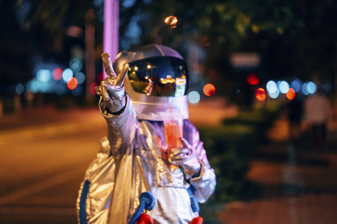 Spaceman in the city at night with takeaway drink making victory gesture stock photo