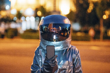Spaceman auf einer Straße in der Stadt in der Nacht hält Smartphone - VPIF00722
