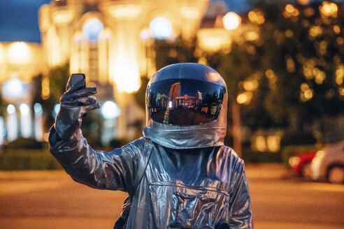 Spaceman auf einer Straße in der Stadt in der Nacht hält Smartphone - VPIF00725