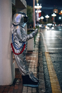 Raumfahrer, der nachts an einer Bushaltestelle steht und ein Handy hält - VPIF00737