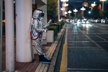 Spaceman standing at a bus stop at night holding cell phone - VPIF00738