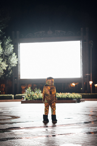 Spaceman on a square at night attracted by shining projection screen stock photo