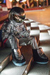 Spaceman sitting on illuminated stairs at night using cell phone - VPIF00761