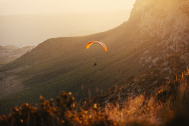 Spanien, Silhouette eines Gleitschirms, der bei Sonnenuntergang hoch über den Bergen schwebt - OCAF00348