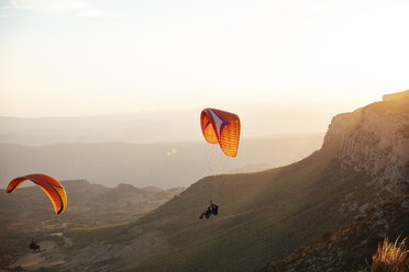Spain, Silhouette of paraglider soaring high above the mountains at sunset - OCAF00349