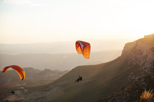 Spanien, Silhouette eines Gleitschirms, der bei Sonnenuntergang hoch über den Bergen schwebt - OCAF00349