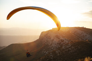 Spain, Silhouette of paraglider soaring high above the mountains at sunset - OCAF00350
