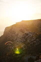 Spain, Silhouette of paraglider soaring high above the mountains at sunset - OCAF00351