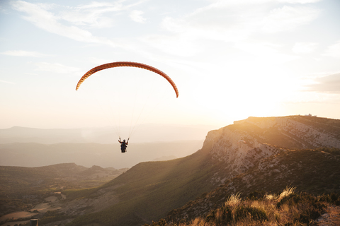 Spanien, Silhouette eines Gleitschirms, der bei Sonnenuntergang hoch über den Bergen schwebt, lizenzfreies Stockfoto