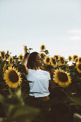 Portrait of a young woman standing in a field of sunflowers, hand in hair - OCAF00353
