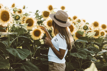 Junge Frau mit Strohhut, stehend in einem Sonnenblumenfeld - OCAF00358