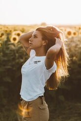 Porträt einer jungen Frau in einem Sonnenblumenfeld, die Hände im Haar - OCAF00367