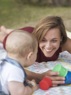 Junge Frau spielt mit einem kleinen Mädchen, das auf einer Decke im Gras liegt - LAF02089
