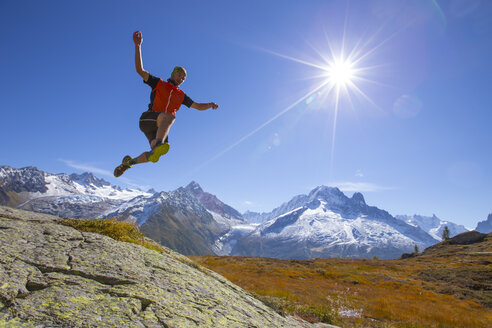Ein junger männlicher Läufer springt auf einem Bergrücken in der Nähe von Chamonix in die Luft, mit dem spektakulären Mont-Blanc-Massiv im Hintergrund. - AURF04590