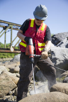 Eine Frau arbeitet mit einem Bohrhammer an einem großen Felsbrocken. - AURF04635
