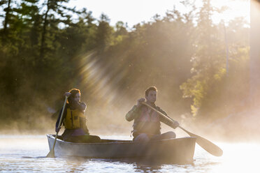 Ein junges Paar paddelt ein Kanu durch Morgennebel auf Long Pond in Maine's North Woods - AURF04663