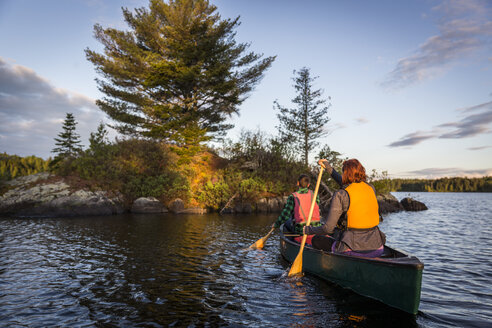 Ein junges Paar paddelt ein Kanu auf Long Pond in den nördlichen Wäldern von Maine in der Nähe von Greenville, Maine - AURF04665