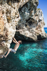 Ein junger Mann klettert auf einen Felsen am Mittelmeer in Cala Varques, Spanien - AURF04674