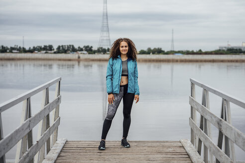 Junge sportliche Frau steht auf einem Steg am Flussufer - VPIF00763