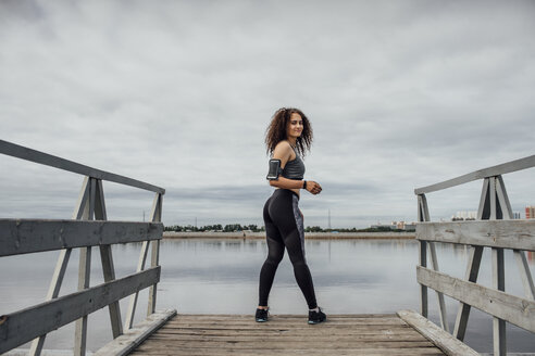 Junge sportliche Frau steht auf einem Steg am Flussufer - VPIF00770