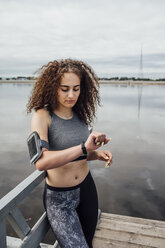 Young athletic woman at the riverside looking at wristwatch - VPIF00771