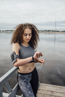 Junge sportliche Frau am Flussufer schaut auf ihre Armbanduhr - VPIF00771