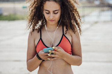Junge sportliche Frau, die Ohrhörer trägt und ein Smartphone benutzt - VPIF00784