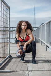 Porträt einer jungen sportlichen Frau mit Ohrstöpseln, die im Freien hockt - VPIF00791