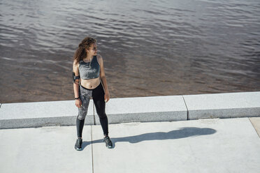 Junge sportliche Frau mit Kopfhörern am Flussufer stehend - VPIF00797