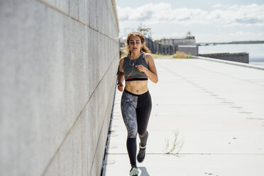Junge sportliche Frau läuft an einer Mauer entlang - VPIF00808
