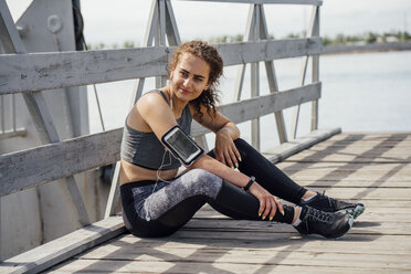 Young athletic woman wearing earbuds resting at the riverside - VPIF00811