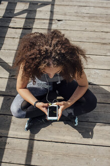 Junge sportliche Frau sitzt auf der Promenade und benutzt ihr Smartphone - VPIF00813